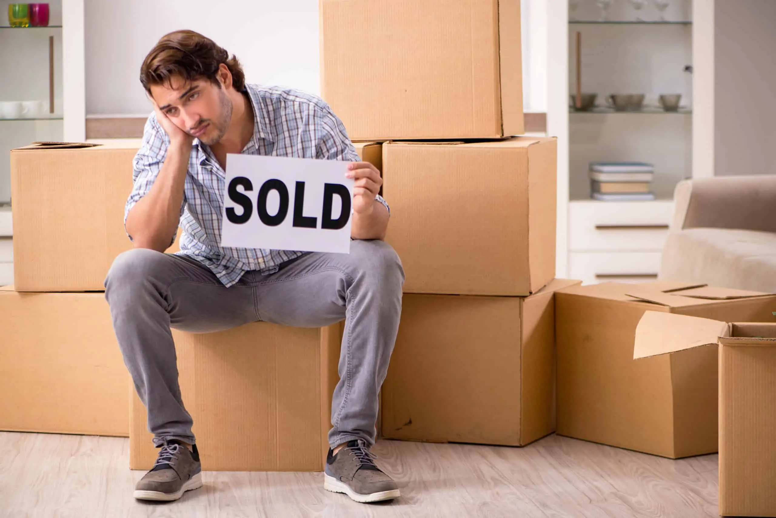 A man sitting on top of boxes, desperate to sell his home.