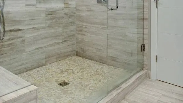 A bathroom with a glass shower stall featuring white tile walls and pebble tile flooring on the shower floors.