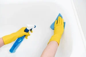 A person wearing yellow gloves cleaning a bathtub in the bathroom to get rid of the urine smell.